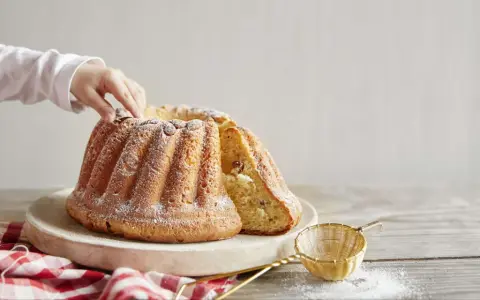 Un enfant touche un Kougelhopf, une des spécialités alsace, saupoudré de sucre glace. Une tranche est coupée, révélant des raisins secs.