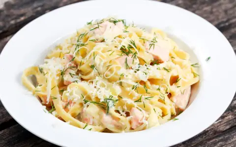 Pyszny makaron z łososiem w kremowym sosie, posypany parmezanem i świeżym koperkiem. Idealny na obiad.
