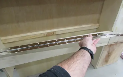 Main tenant une longue charnière piano pour la fixer sur un meuble en bois.