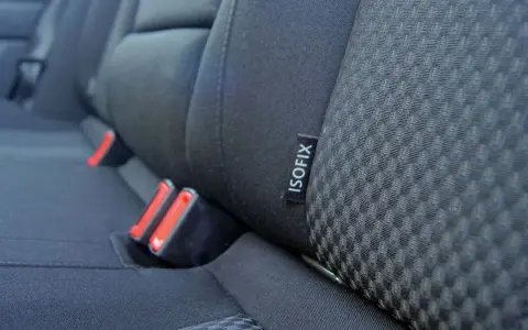 Etiqueta negra con el **símbolo ISOFIX** en el asiento de un coche, junto a los anclajes de seguridad.