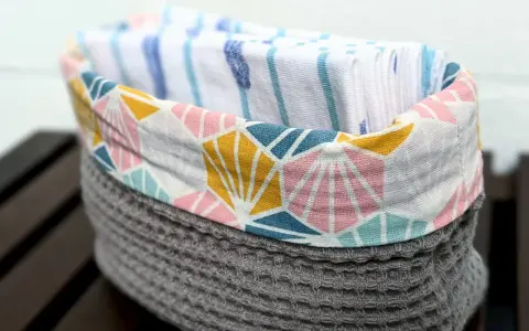 Un panier en tissu gris avec un motif géométrique coloré contient des mouchoirs en tissu. Une idée pour savoir que faire avec des mouchoirs en tissu.