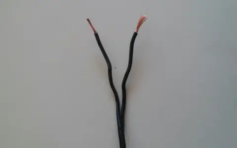 Dwa czarne przewody elektryczne rozchodzą się, odsłaniając miedziane końcówki. Czy czerwony to plus czy minus?
