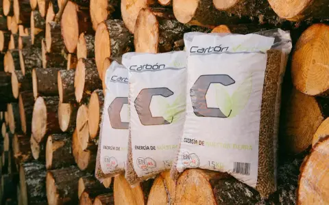 Bolsas de pellets de madera "Carbón Verde" apiladas contra troncos. Si tu estufa de pellets muestra un error 3, revisa la carga de combustible.