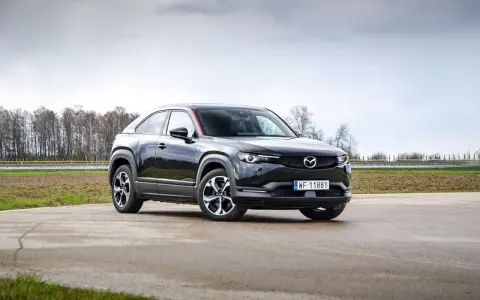 Czarna Mazda MX-30 na tle pochmurnego nieba i drzew.