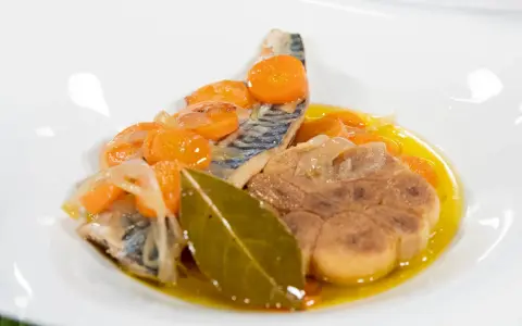 Deliciosa caballa en escabeche con zanahorias, cebolla y laurel en un plato blanco.