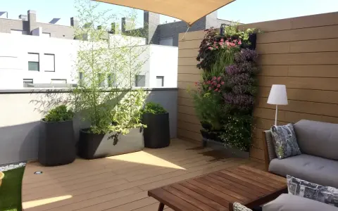 Un **jardín moderno** en una terraza con sofá, mesa de madera, plantas en macetas y un muro verde vibrante.