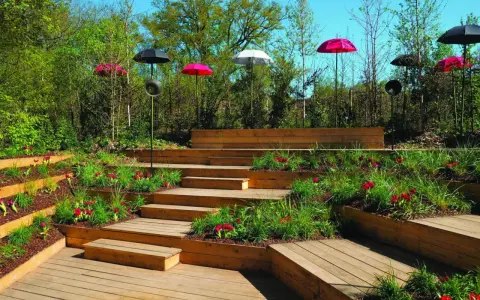 Aménagement de jardins avec terrasses en bois, parterres fleuris et parasols colorés.