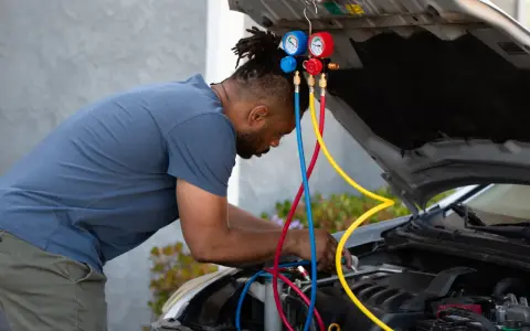 Man working on car engine, using gauges and hoses to fix car AC.