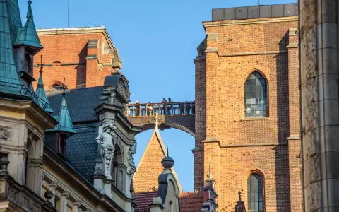 Most zabytkowych budynków we Wrocławiu z ludźmi na moście i wieżą Katedry w tle.