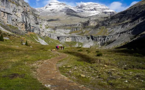 Wanderer auf einem Pfad im Ordesa Nationalpark, umgeben von steilen Felswänden und schneebedeckten Gipfeln.