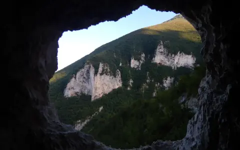 Vista dalla **grotta nera** su un monte verdeggiante con rocce bianche affioranti.