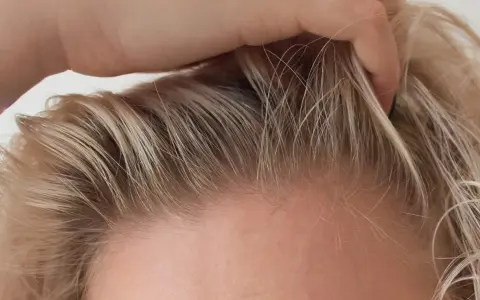Dłoń delikatnie przeczesuje jasne włosy, ukazując drobne kosmyki, które zdradzają, jak ujarzmić baby hair.