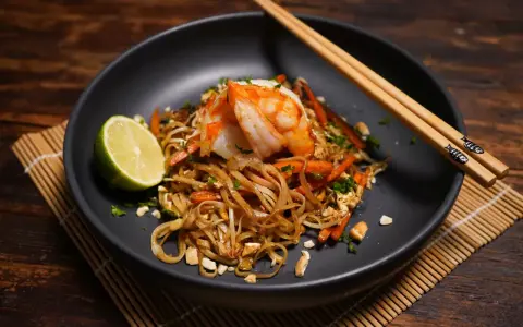 Ein Teller Pad Thai mit Garnelen, Limette und Erdnüssen, bereit zum Genießen.