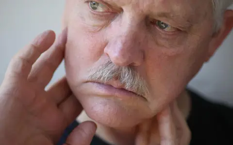 Mann mit Schnurrbart, der sich mit den Fingern das Gesicht berührt, als ob er ein Kribbeln im Gesicht spürt.