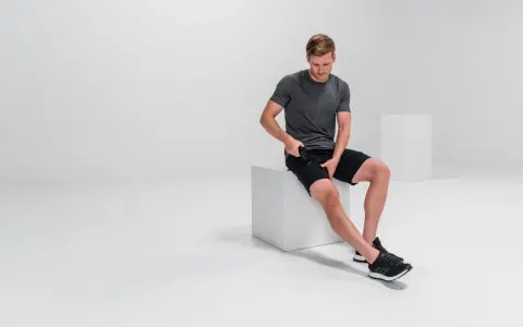 Mann massiert mit Massagepistole seine Oberschenkel, um adduktoren schmerzen zu lindern.