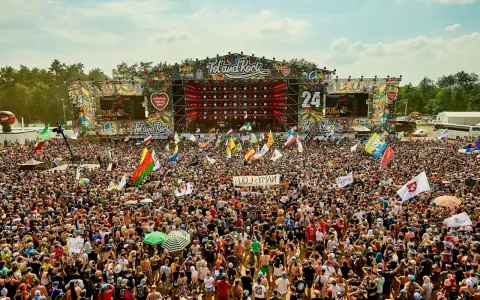 Tłum ludzi na festiwalu Poland Rock, gdzie jest scena i ekrany. Wszędzie flagi i słońce.