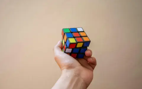 En hand håller en färgglad rubiks kub nyckelring mot en ljus bakgrund.