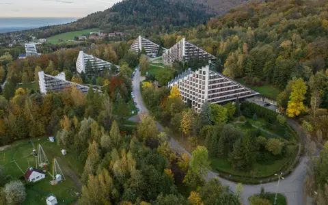 Widok z lotu ptaka na sanatoria o trójkątnej architekturze w otoczeniu jesiennego lasu.