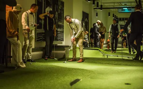 Människor i festliga kläder spelar minigolf på Golfbaren Stockholm.