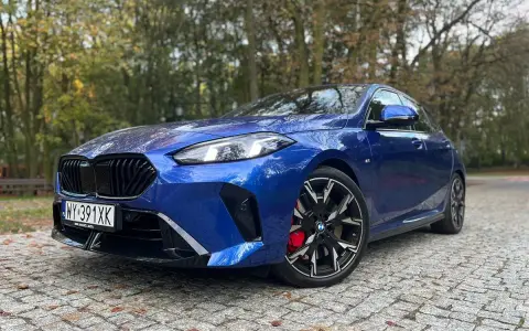 Błękitne, sportowe niemieckie auto BMW z czarnymi felgami i czerwonymi zaciskami hamulcowymi stoi na brukowanej drodze wśród jesiennych drzew.