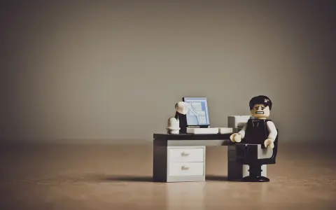 Figurka Lego przedstawiająca zestresowanego pracownika siedzącego przy biurku z komputerem.