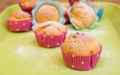Leckere Muffins ohne Ei, bestäubt mit Puderzucker, in bunten Papierförmchen auf hellgrüner Unterlage.