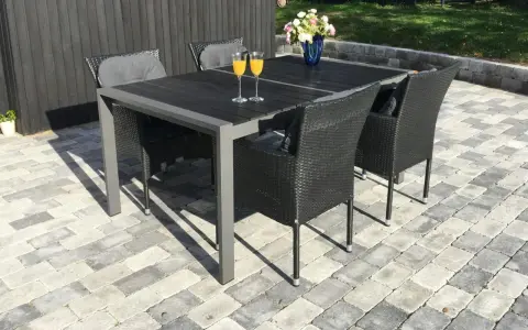 En uteplats med stenläggning, ett mörkt bord med korgstolar och glas med juice.