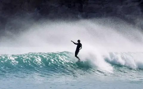 Surfer in Aktion auf einer Welle an der Algarve. Die Gischt spritzt, während er die portugiesische Küste genießt.
