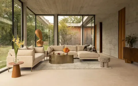 Sofá seccional beige y sillón en un salón moderno con grandes ventanales. Las combinaciones con beige crean un ambiente sereno y elegante.