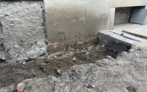 Prace przy wzmocnieniu fundamentów w starym domu. Widoczne wykopy, odsłonięta ściana i nowe elementy betonowe.