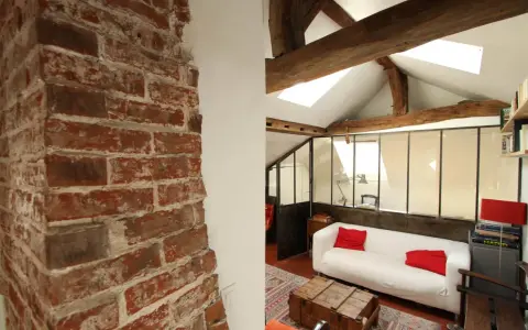 Aménagement combles idées : un salon cosy sous les toits avec murs en briques apparentes, poutres en bois et canapé blanc.
