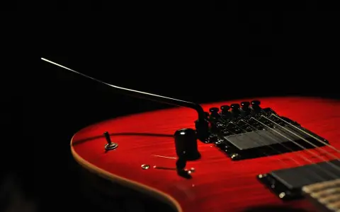 Czerwona gitara elektryczna z czarnym mostkiem tremolo, gotowa do wydobycia dźwięków, które poruszą serce.