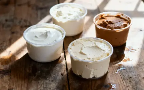 Composition de quatre pots de produits laitiers crémeux, dont une ricotta au chocolat, sur une table en bois rustique.