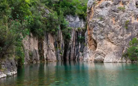 Aguas cristalinas reflejan imponentes rocas y vegetación exuberante en estas piscinas naturales de Castellón. Un rincón idílico para refrescarse.
