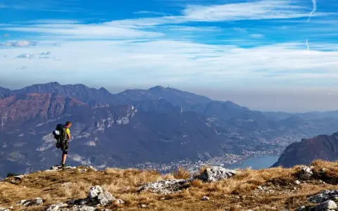 Escursionista ammira la vista panoramica di una montagna vicino Milano, con un lago e un paese in lontananza.