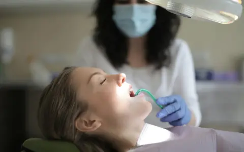 Pacjentka u dentysty, która ma w ustach zieloną końcówkę ssaka stomatologicznego.