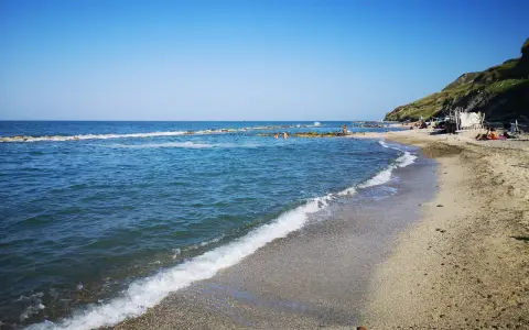 La **spiaggia** di **Castel di Mezzo** baciata dal sole, con il mare azzurro e la collina verde sullo sfondo.