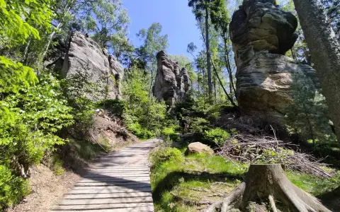 Drewniana ścieżka prowadzi przez skalne miasto w Górach Stołowych Czech. Majestatyczne formacje skalne otoczone zielenią.