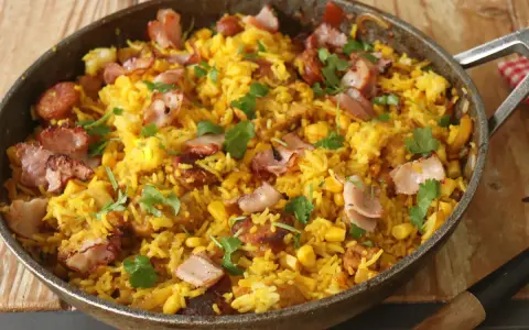 Arroz paisa en sartén, con trozos de tocino crujiente, maíz y cilantro fresco. ¡Un festín para los sentidos!