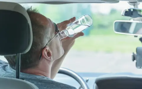 Mężczyzna pije alkohol za kierownicą. Pamiętaj, jaka kara za jazdę pod wpływem alkoholu jest surowa.