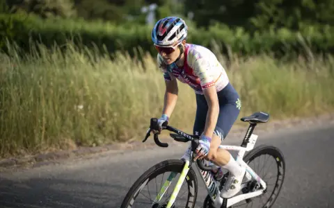 Elise Chabbey in voller Fahrt auf ihrem Rennrad, die Konzentration im Blick, während sie durch eine grüne Landschaft fährt.