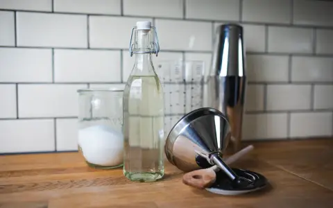Zutaten für zuckersirup selber machen: Zucker in einem Glas, Sirup in einer Flasche, Cocktail-Shaker und Trichter.