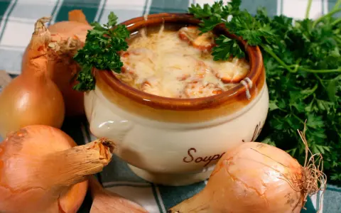 Un bol de soupe à l'oignon gratinée, un plat parisien réconfortant, entouré d'oignons frais et de persil.