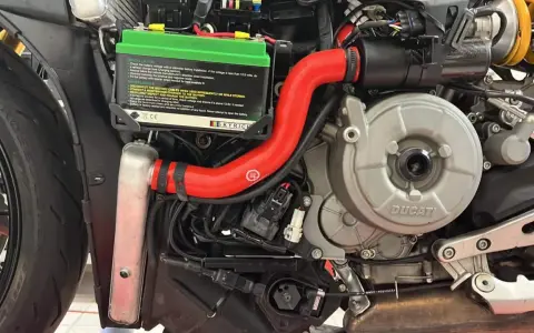 Dettaglio del sistema di raffreddamento motore di una Ducati, con radiatore, tubi rossi e motore in vista.