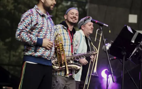 Adam Kłosiński z zespołem na scenie, grają na saksofonie i puzonie.