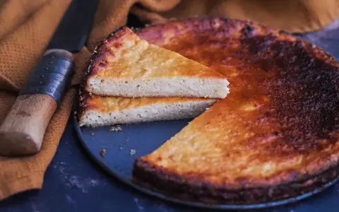 Un fiadone corse, un gâteau au fromage et au citron, est servi avec une tranche coupée, à côté d'un couteau sur un tissu ocre.
