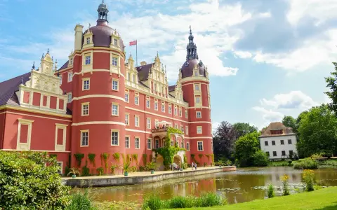Piękny czerwony zamek otoczony wodą i zielenią. Idealne miejsce na zwiedzanie parku mużakowskiego.