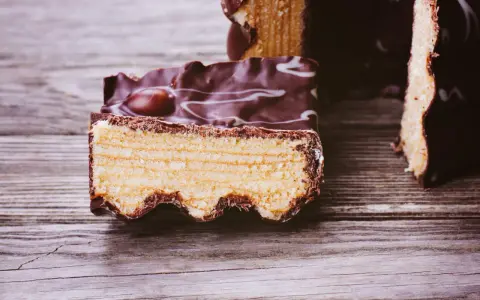 Ein Stück Baumkuchen mit Schokoladenglasur und weißen Zuckerguss-Wirbeln, perfekt für ein Baumkuchen Rezept.