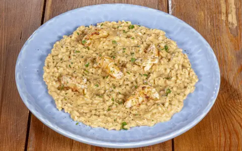Un cremoso risotto alla crema di scampi, guarnito con scampi scottati e prezzemolo tritato, servito su un piatto azzurro.