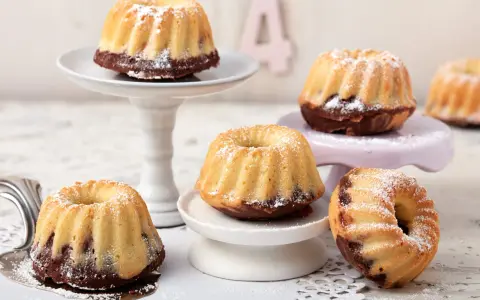 Mehrere mini Gugelhupf mit Puderzucker bestäubt, auf verschiedenen Etageren arrangiert.